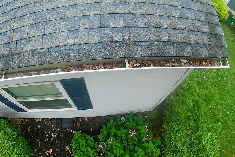 Shingle grit and leaf litter filling a front gutter before cleaning in Limerick, PA